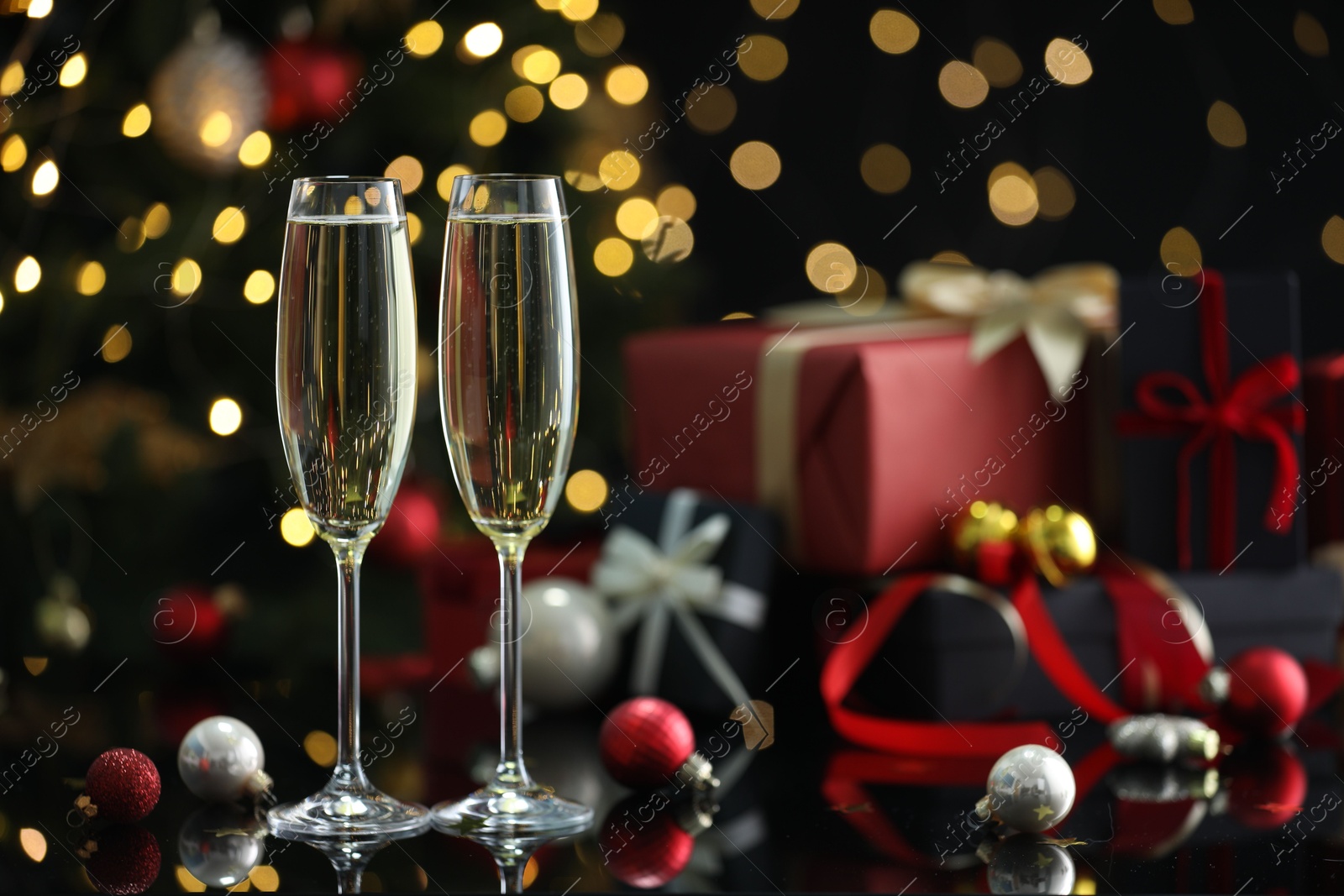 Photo of Delicious champagne in glasses and Christmas decor on black mirror surface against blurred lights, closeup. Space for text