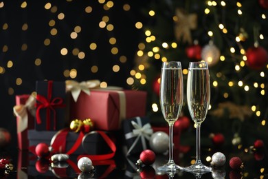 Photo of Delicious champagne in glasses and Christmas decor on black mirror surface against blurred lights. Space for text