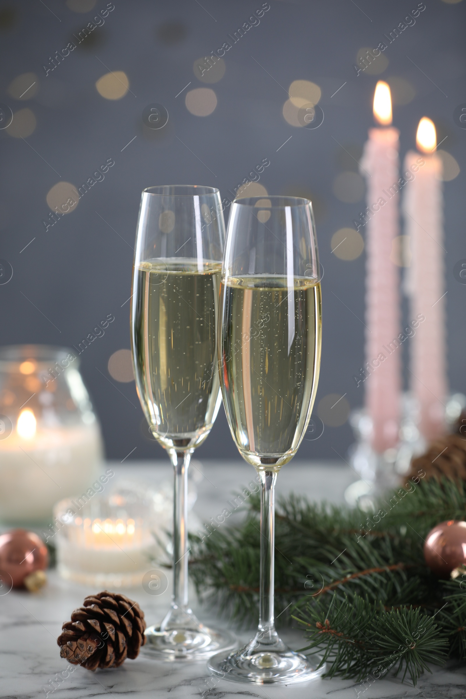 Photo of Delicious champagne in glasses and Christmas decor on marble table against blurred lights, closeup