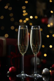 Photo of Delicious champagne in glasses and baubles on black mirror surface against blurred lights. Christmas celebration