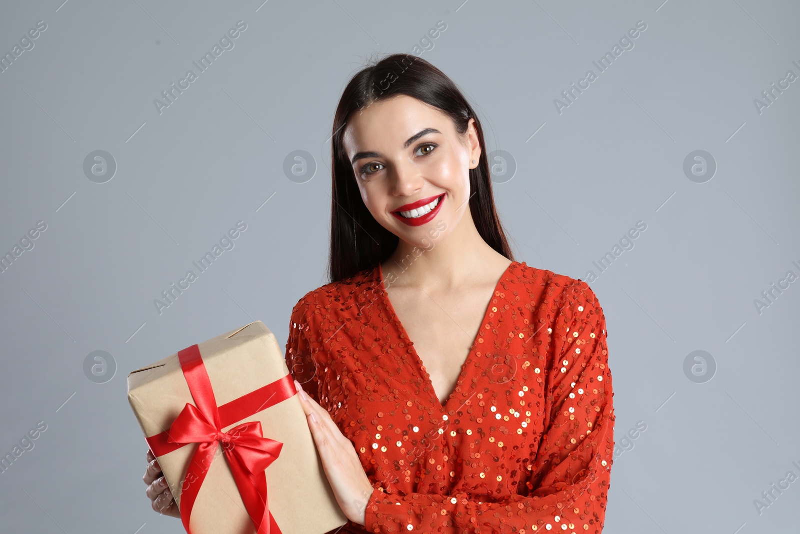 Photo of Woman in red dress holding Christmas gift on grey background