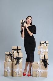 Photo of Woman in black dress with Christmas gifts on grey background