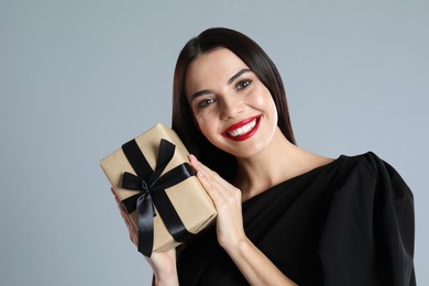 Photo of Woman in black dress holding Christmas gift on grey background