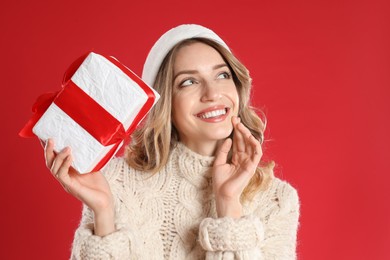 Photo of Beautiful young woman in Santa hat with Christmas present on red background