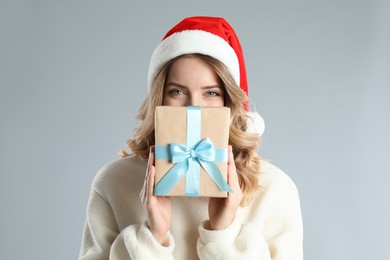 Photo of Beautiful young woman in Santa hat with Christmas present on light grey background