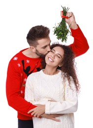 Happy man kissing his girlfriend under mistletoe bunch on white background