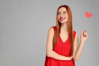 Photo of Young woman in red dress with paper heart on light grey background, space for text