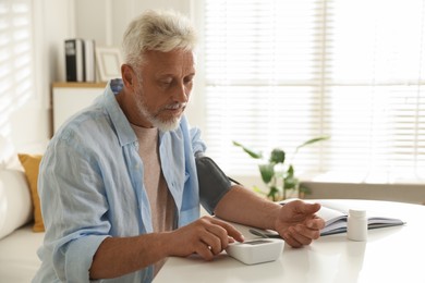 Senior man measuring blood pressure at table indoors