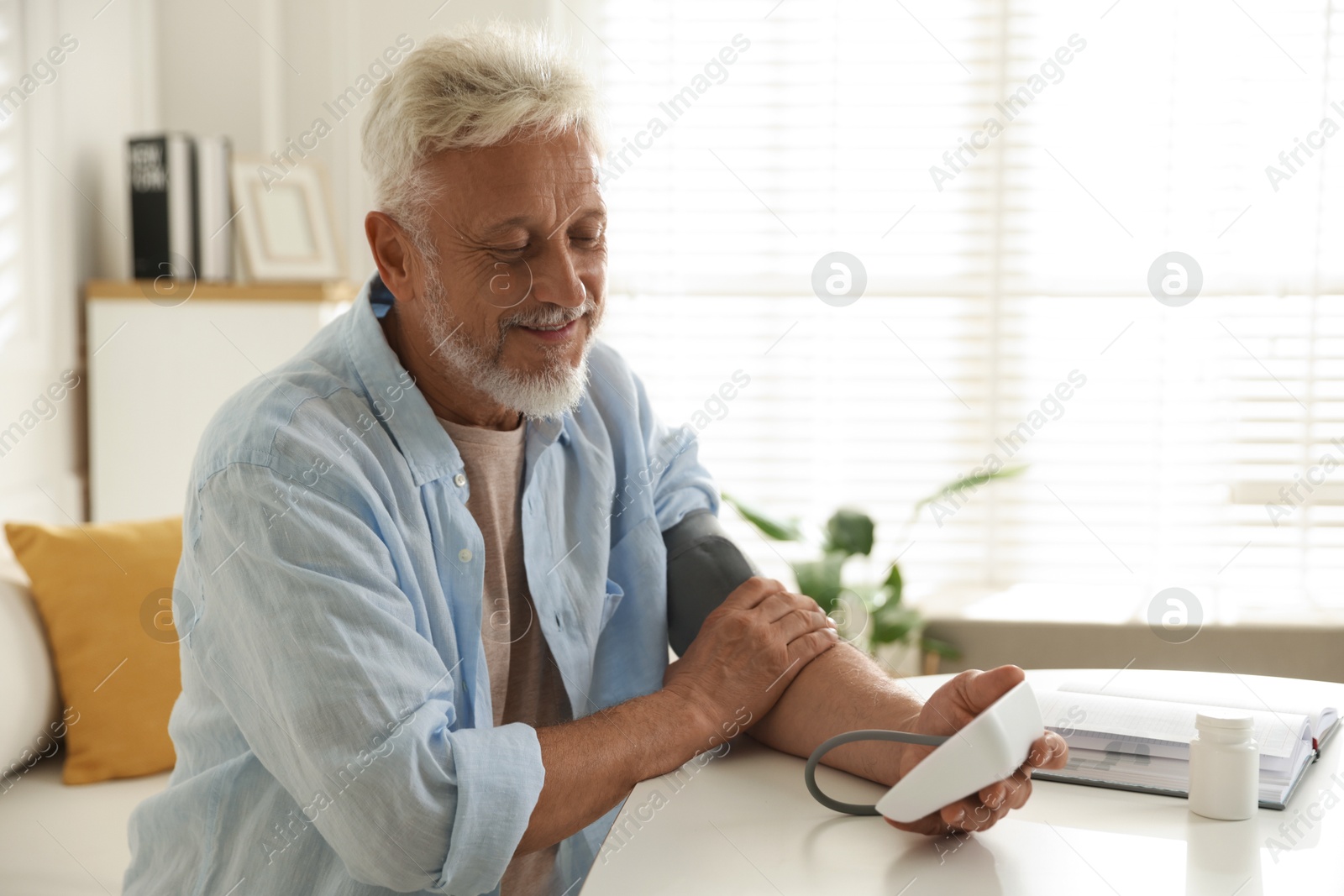 Photo of Senior man measuring blood pressure at table indoors