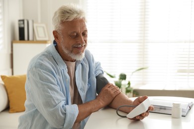 Photo of Senior man measuring blood pressure at table indoors