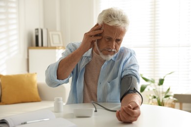 Photo of Senior man measuring blood pressure at table indoors