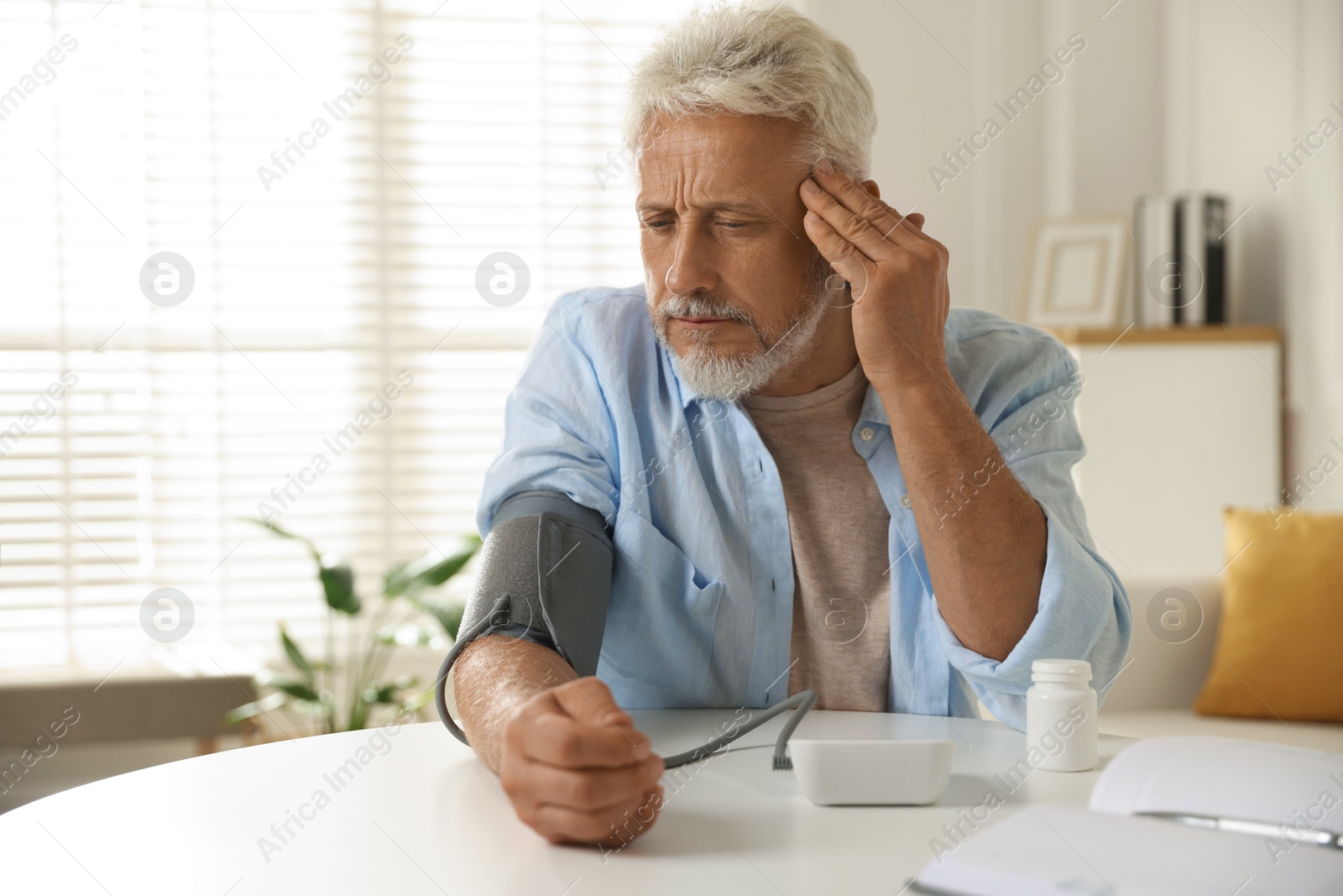 Photo of Senior man measuring blood pressure at table indoors