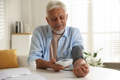 Photo of Senior man measuring blood pressure at table indoors