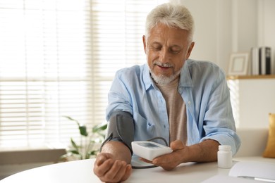 Photo of Senior man measuring blood pressure at table indoors