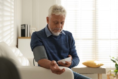 Photo of Senior man measuring blood pressure on sofa indoors