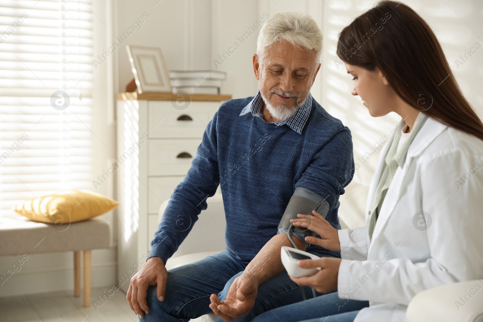 Photo of Doctor measuring patient's blood pressure on sofa indoors