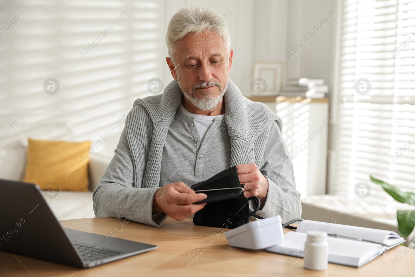 Photo of Senior man measuring blood pressure at wooden table indoors