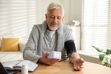 Photo of Senior man measuring blood pressure at wooden table indoors