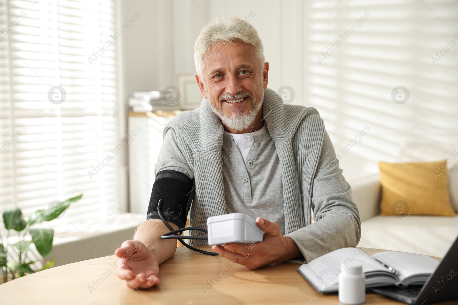 Photo of Senior man measuring blood pressure at wooden table indoors