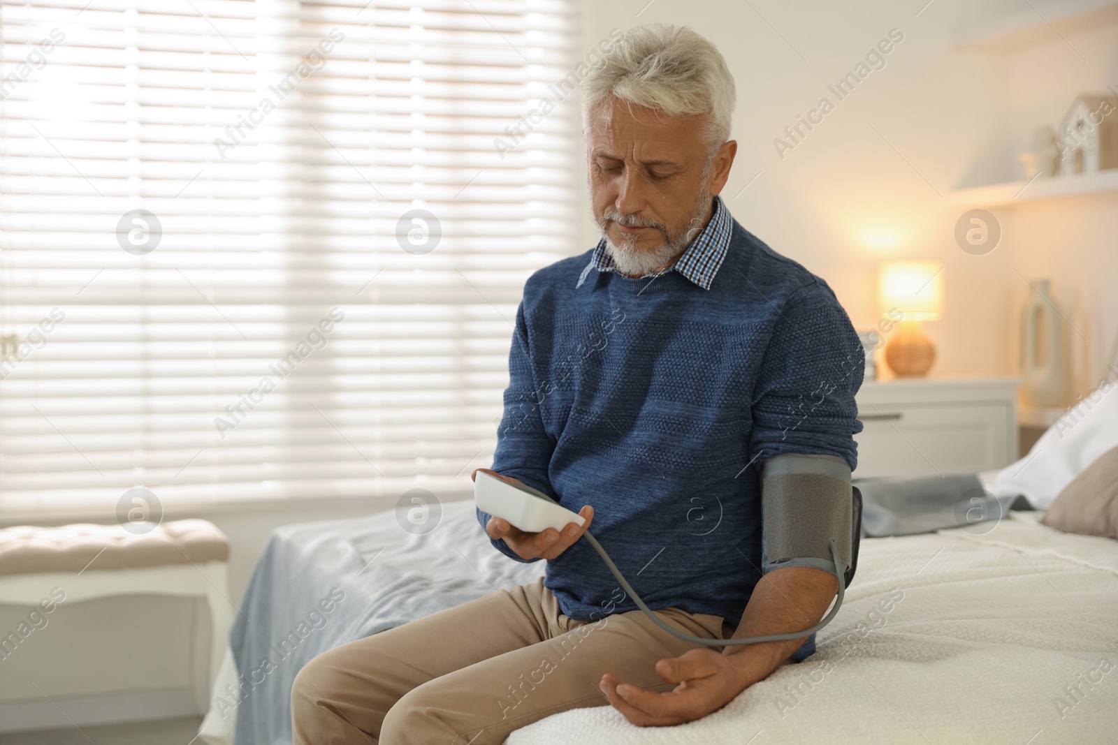 Photo of Senior man measuring blood pressure on bed indoors