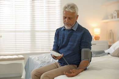 Senior man measuring blood pressure on bed indoors