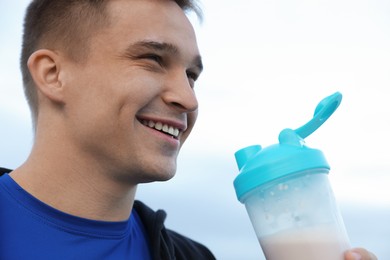 Photo of Smiling man with shaker of protein drink outdoors, closeup