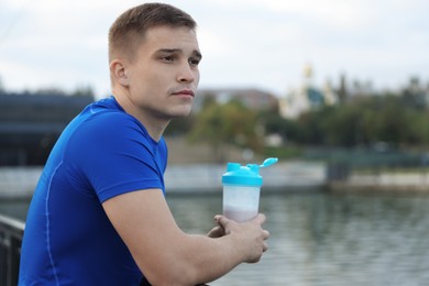 Photo of Athletic man with shaker of protein drink outdoors. Space for text