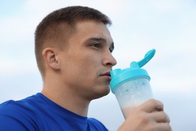 Photo of Handsome athletic man drinking protein shake outdoors, closeup