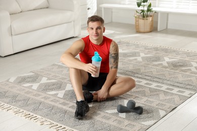 Photo of Athletic man with shaker of protein drink sitting on carpet at home