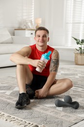 Photo of Athletic man with shaker of protein drink sitting on carpet at home