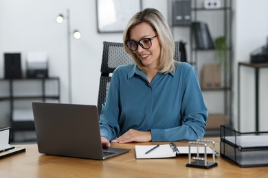 Happy businesswoman working on laptop at table in office