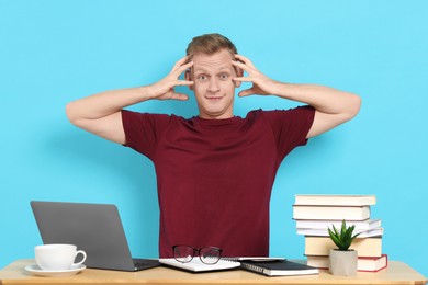 Photo of Preparing for exam. Student with laptop and books at table against light blue background