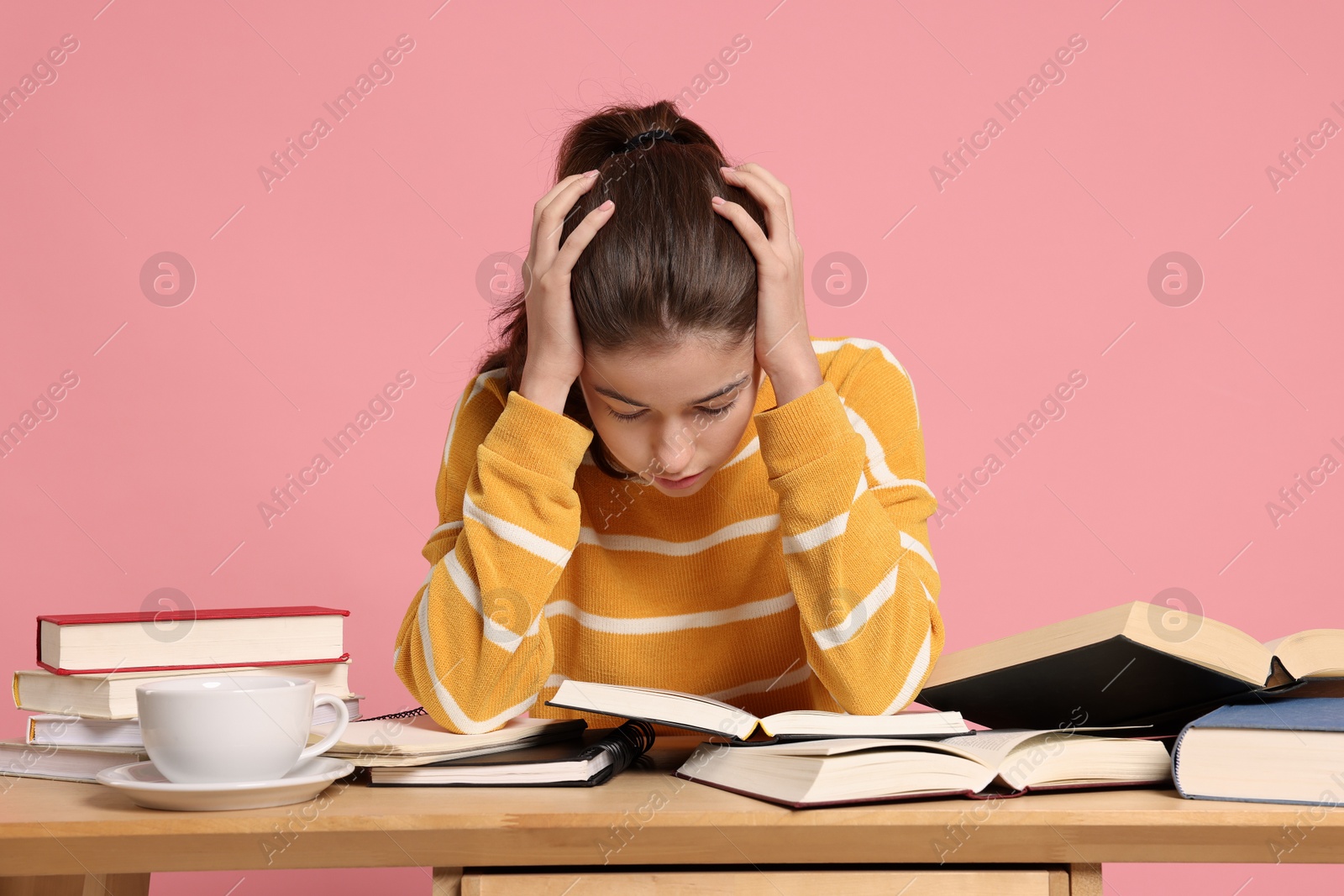 Photo of Preparing for exam. Student with books at table against pink background