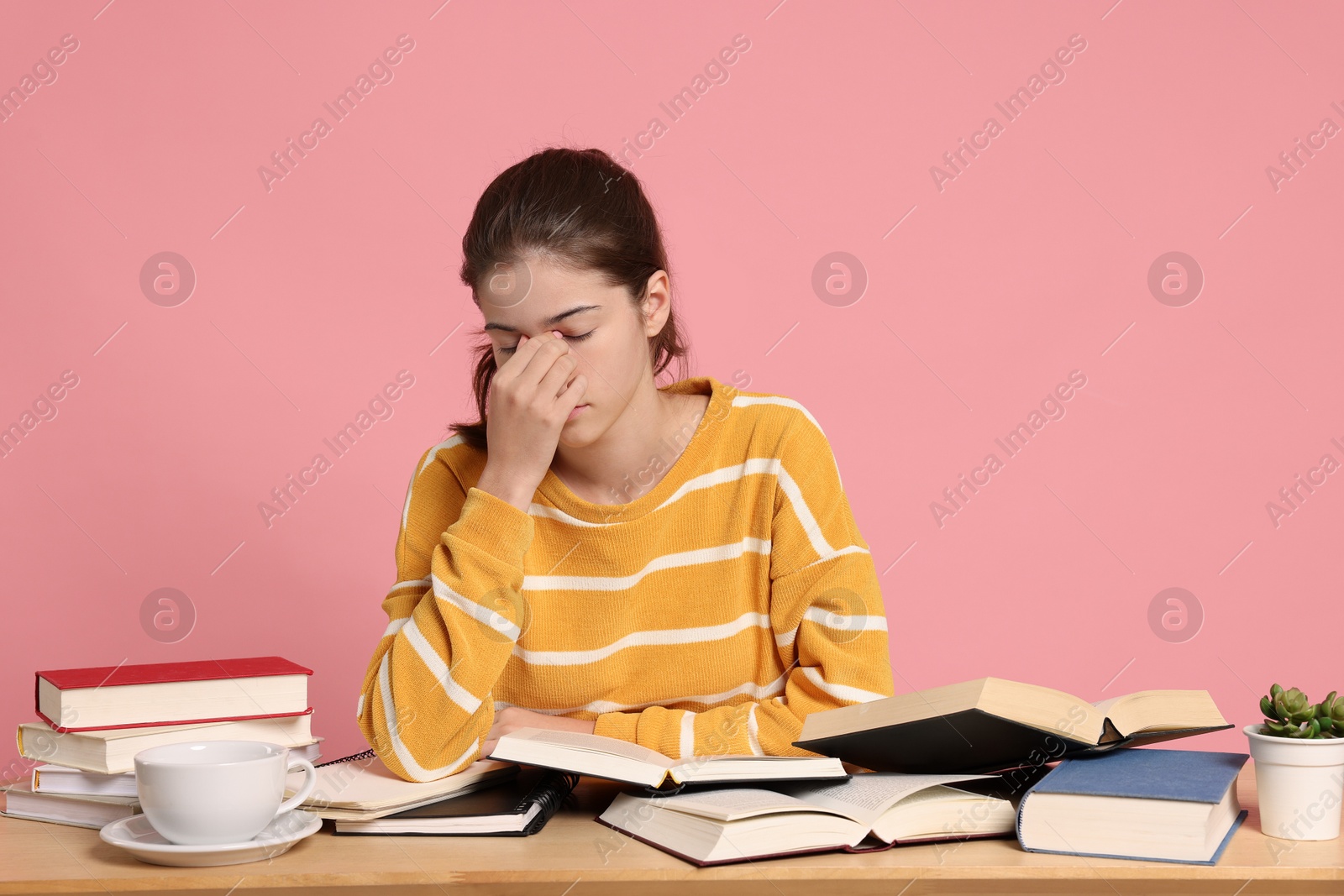 Photo of Preparing for exam. Tired student with books at table against pink background