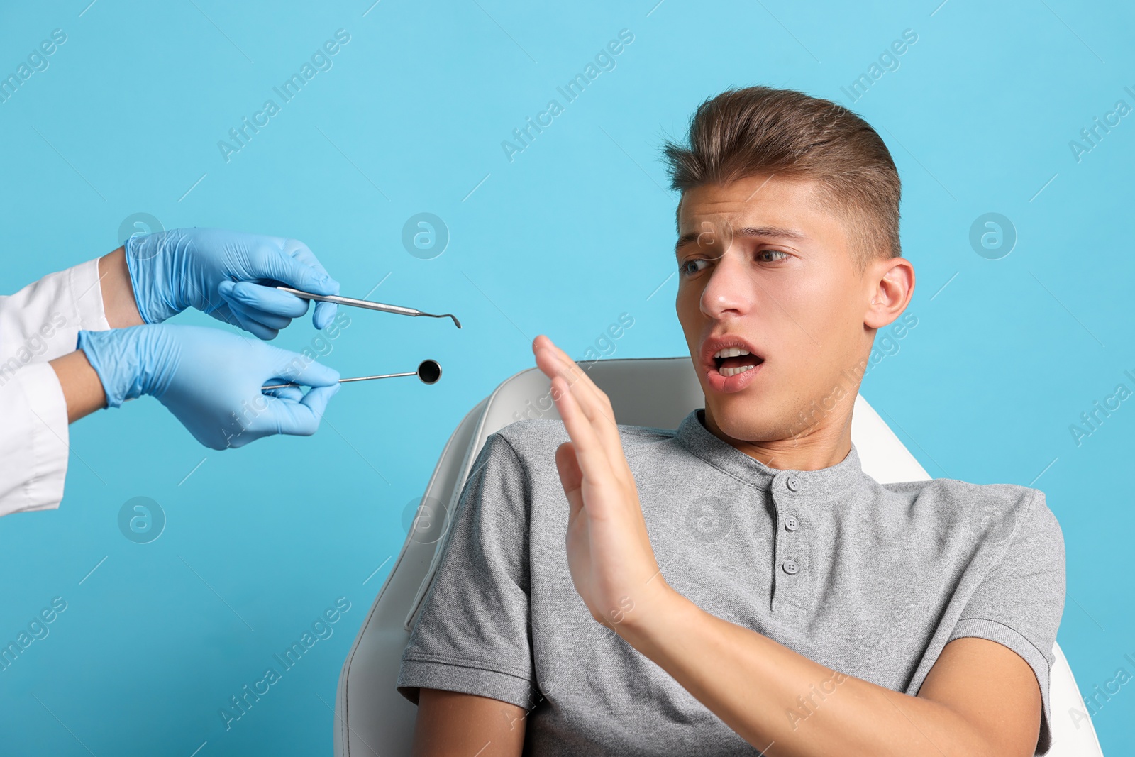 Photo of Dental phobia. Dentist working with scared man on light blue background, closeup