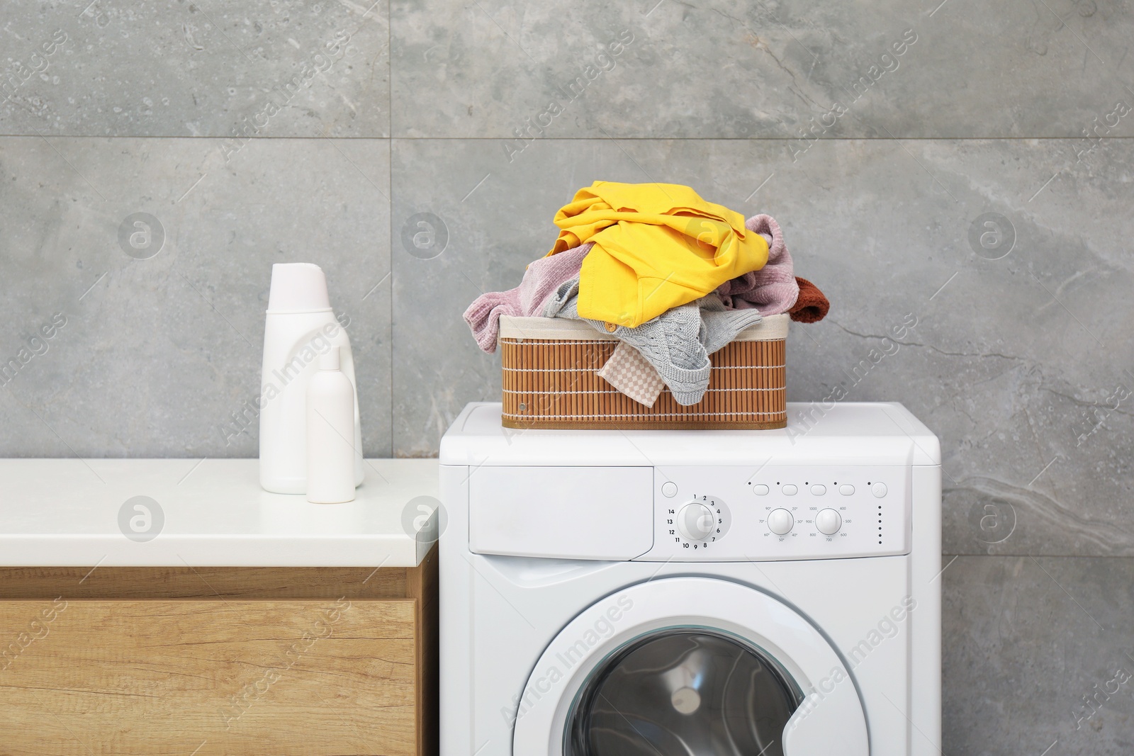 Photo of Detergents, basket with laundry and washing machine in bathroom