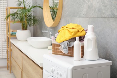 Photo of Detergents and basket with laundry on washing machine in bathroom