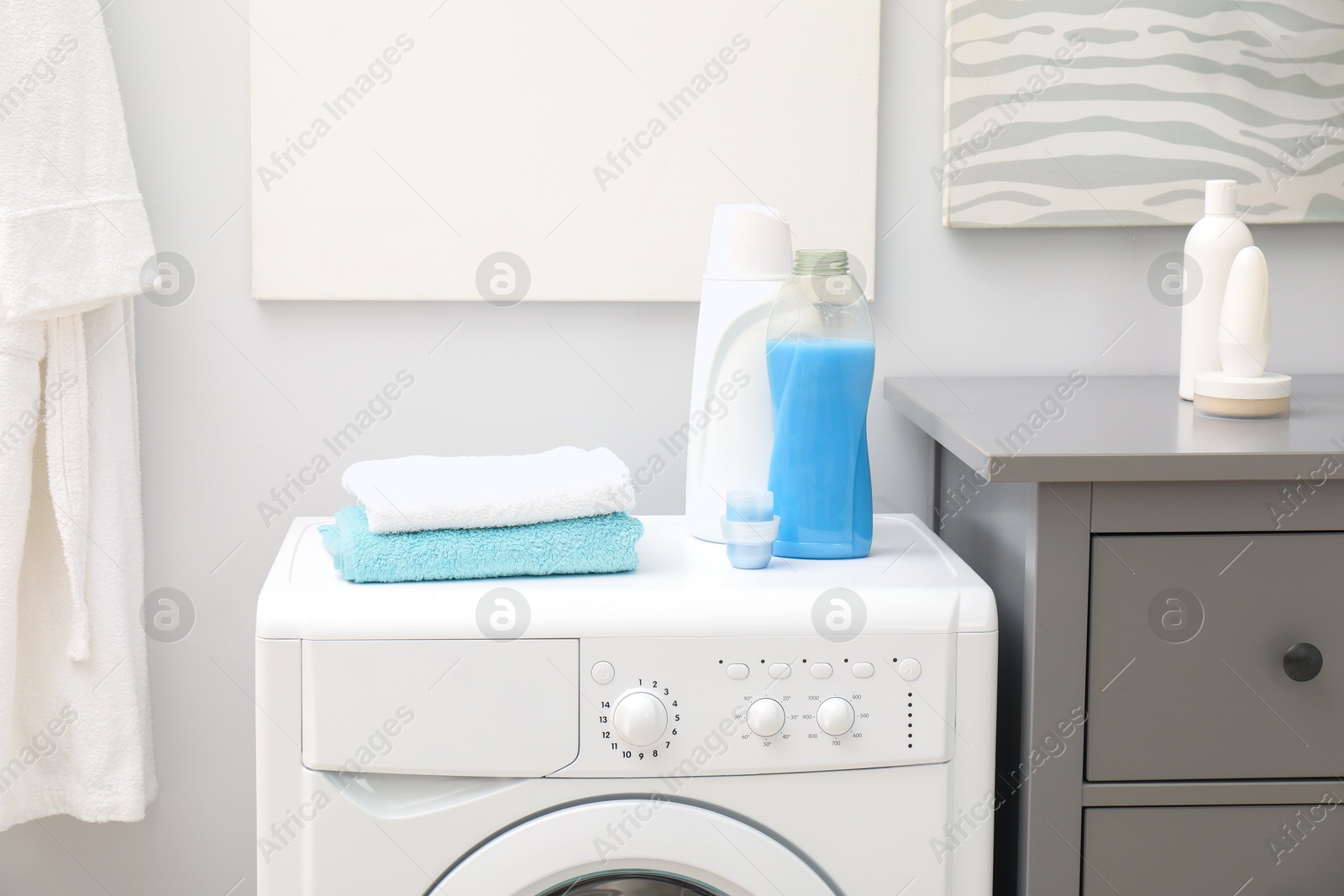 Photo of Laundry detergents and clean terry towels on washing machine in bathroom