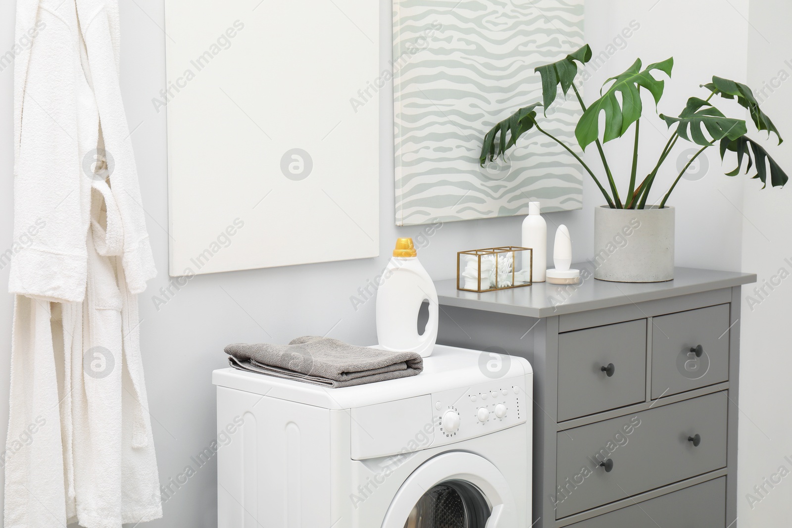 Photo of Laundry detergent and clean terry towel on washing machine in bathroom