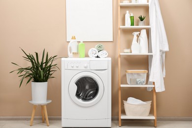 Photo of Laundry detergents, terry towels, washing machine and decorative ladder in bathroom