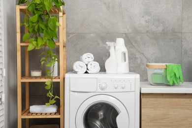 Photo of Laundry detergents, terry towels, washing machine and shelving unit in bathroom