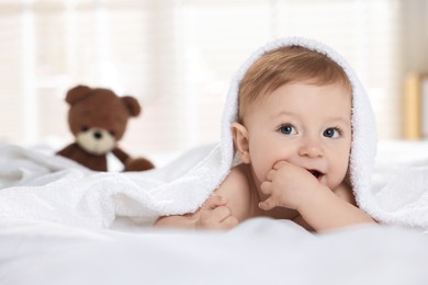 Cute baby under terry towel lying on bed at home