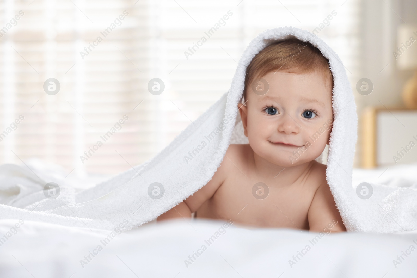 Photo of Cute baby under terry towel lying on bed at home