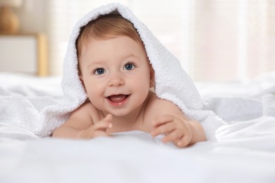 Photo of Cute baby under terry towel lying on bed at home