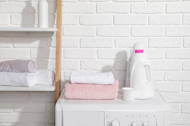 Photo of Laundry detergents, cap and stacked clean towels on washing machine in bathroom