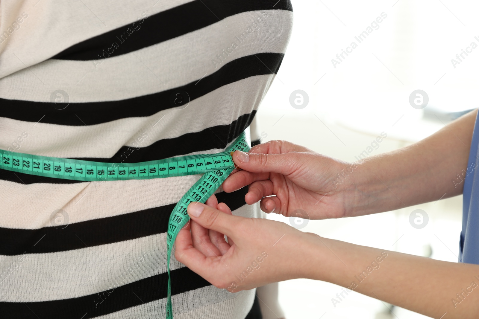 Photo of Nutritionist measuring overweight woman's waist with tape in hospital, closeup