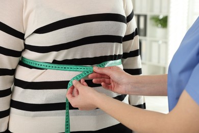 Nutritionist measuring overweight woman's waist with tape in hospital, closeup