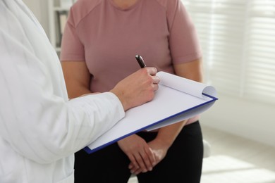 Photo of Nutritionist with clipboard giving recommendations to overweight woman in hospital, closeup