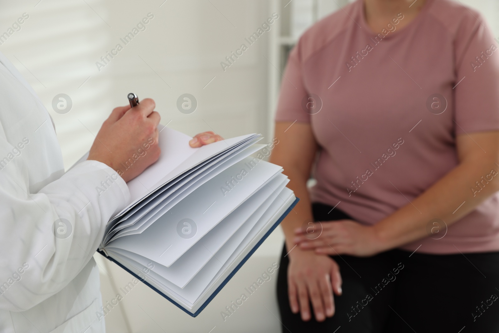 Photo of Nutritionist with notebook giving recommendations to overweight woman in hospital, closeup