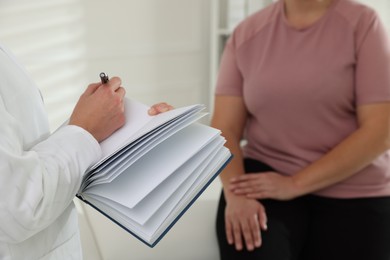 Photo of Nutritionist with notebook giving recommendations to overweight woman in hospital, closeup